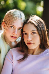 Tender teen sisters looking at camera on sunny summer day in green garden - ADSF29241