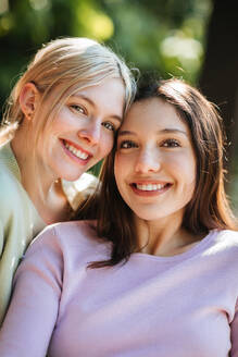 Zarte, fröhliche Teenager-Schwestern schauen in die Kamera an einem sonnigen Sommertag im grünen Garten - ADSF29242
