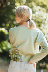 Rückenansicht eines Teenagers mit Wildblumen in der Jeanstasche im Sommerpark - ADSF29244