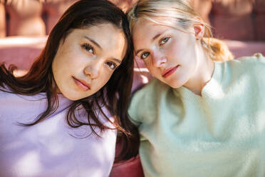 Gentle teen sisters sitting near comfortable couch in garden on sunny day and looking at camera - ADSF29247