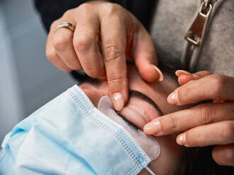 Crop anonymous beauty master applying lash lift shield on eyelid of female client during eyelash treatment in salon - ADSF29273