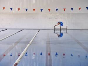 Seitenansicht eines Trainers, der seinen Körper streckt und seine Knie umarmt, während er eine Übung im Wasseraerobic-Training im Pool durchführt - ADSF29277