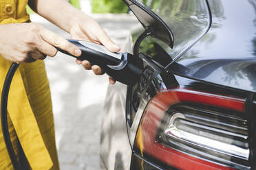 Mature woman holding cable by plug of electric car - JCCMF03720