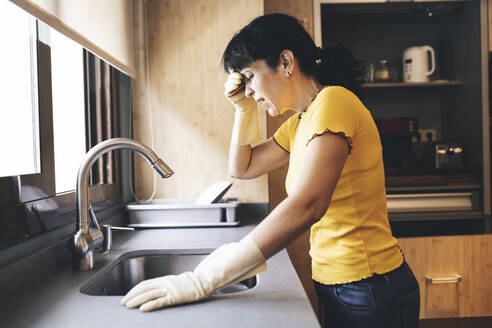 Müde Frau steht bei Utensilien an der Küchenspüle zu Hause - JCCMF03763