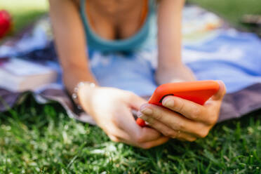 Nahaufnahme einer anonymen Person, die ein Telefon benutzt, während sie an einem Sommertag im Gras liegt - ADSF29296