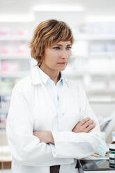 Female pharmacist standing with arms crossed at pharmacy - JOSEF05395