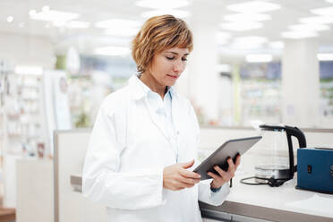 Female pharmacist using digital tablet while standing at medical store - JOSEF05397
