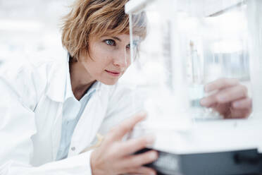 Female pharmacist looking at medical equipment in glass box - JOSEF05401