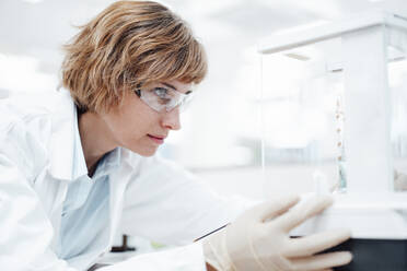 Female professional with protective eyewear checking equipment at pharmacy - JOSEF05402