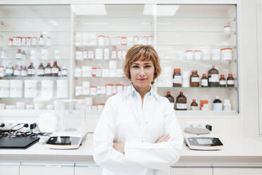 Confident female pharmacist with arms crossed standing at pharmacy - JOSEF05409