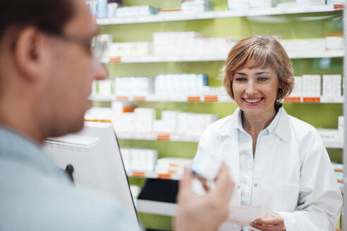 Lächelnde Apothekerin, die einen Kunden bei der Überprüfung von Medikamenten beobachtet - JOSEF05416