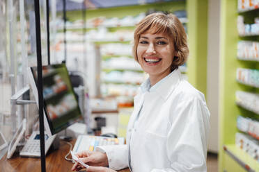 Happy female pharmacist standing in medical store - JOSEF05419