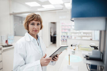 Female professional holding digital tablet while standing at laboratory - JOSEF05421