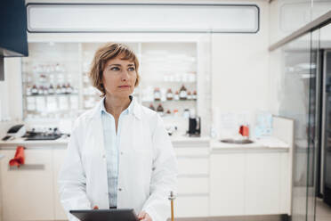 Thoughtful female professional standing at pharmacy - JOSEF05422