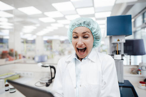 Surprised female pharmacist using digital tablet while standing at laboratory - JOSEF05428