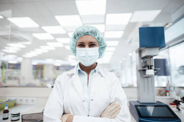 Female pharmacist with arms crossed standing at pharmacy store during pandemic - JOSEF05430