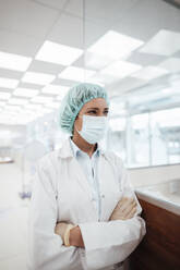 Female pharmacist looking away while standing with arms crossed at pharmacy store during COVID-19 - JOSEF05431