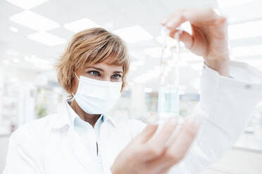 Female pharmacist wearing protective face mask analyzing at laboratory - JOSEF05441