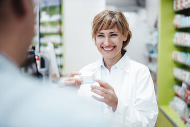 Smiling female pharmacist discussing with male customer at pharmacy store - JOSEF05456