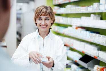 Smiling female pharmacist explaining medicine to male customer at pharmacy store - JOSEF05460