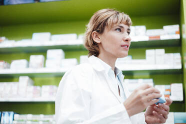 Female pharmacist with short hair holding medicine at pharmacy store - JOSEF05462