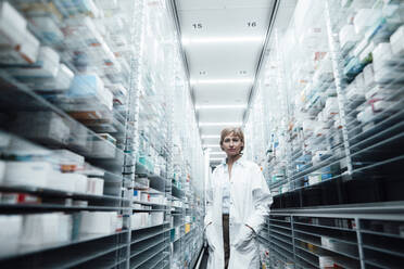 Female pharmacist with hands in pockets standing at pharmacy store - JOSEF05472