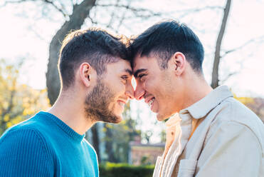 Seitenansicht eines entzückten homosexuellen Paares von Männern, die sich im Park die Nasen berühren und sich gegenseitig ansehen - ADSF29367