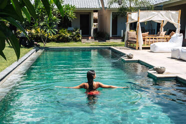 Rückenansicht einer anonymen weiblichen Touristin im Badeanzug, die während eines Sommerausflugs in einem gekräuselten Pool schwimmt - ADSF29406