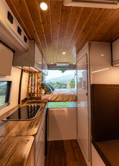 Modern interior of kitchen and bedroom in van parked on meadow in nature - ADSF29408
