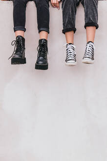 Unerkennbare Frauen in modischen Jeans und Schuhen, die auf einer grauen Wand in einer Stadtstraße sitzen - ADSF29413