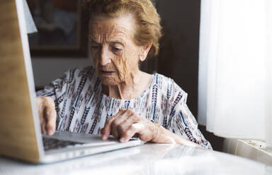 Ältere Frau mit kurzen Haaren benutzt Laptop zu Hause - JCCMF03773
