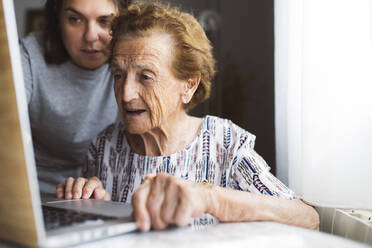 Enkelin hilft der Großmutter bei der Benutzung des Laptops zu Hause - JCCMF03774