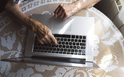 Elderly woman typing on laptop at home - JCCMF03776