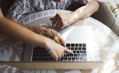 Young woman assisting grandmother using laptop at table - JCCMF03777