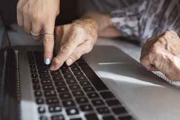 Young granddaughter teaching laptop to grandmother at home - JCCMF03778