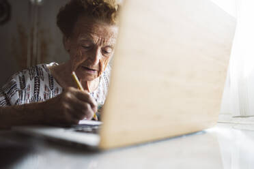 Frau beim Schreiben mit Laptop zu Hause sitzend - JCCMF03781