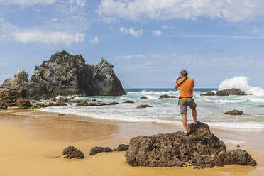 Männlicher Tourist beim Fotografieren von Vulkangestein am Haywards Beach - FOF12153