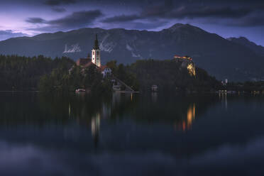 Spectacular scenery of calm pond with island and castle located in rocky highlands in Slovenia during sunset - ADSF29425