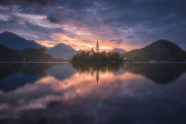 Spektakuläre Kulisse eines ruhigen Teichs mit Insel und Burg in den felsigen Bergen Sloweniens bei Sonnenuntergang - ADSF29426