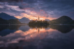 Spectacular scenery of calm pond with island and castle located in rocky highlands in Slovenia during sunset - ADSF29426