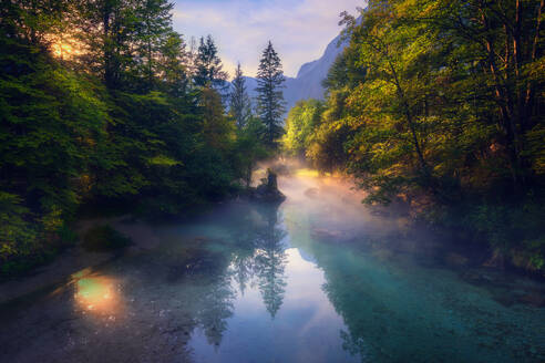 Wunderbare Landschaft von Nebel über ruhigen Fluss in bergigen Wäldern am Morgen in Slowenien gelegen - ADSF29427