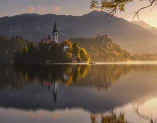 Spectacular scenery of calm pond with island and castle located in rocky highlands in Slovenia during sunset - ADSF29428