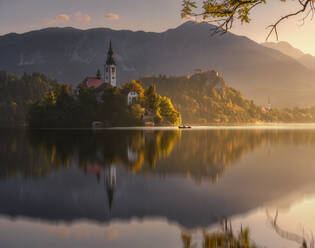 Spektakuläre Kulisse eines ruhigen Teichs mit Insel und Burg in den felsigen Bergen Sloweniens bei Sonnenuntergang - ADSF29428