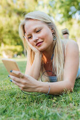 Lächelnd charmante weibliche liegend auf Gras im Park und hören Musik in Kopfhörern im Sommer - ADSF29433