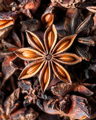 Closeup of aromatic dried anise stars with seeds scattered on rustic wooden table for gastronomy concept background - ADSF29440