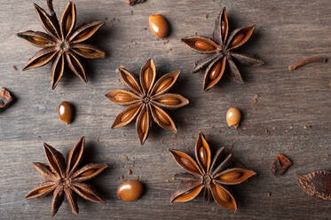 Closeup of aromatic dried anise stars with seeds scattered on rustic wooden table for gastronomy concept background - ADSF29441