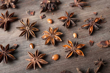 Closeup of aromatic dried anise stars with seeds scattered on rustic wooden table for gastronomy concept background - ADSF29442