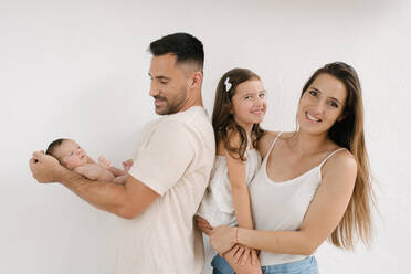 Delighted couple with naked infant and cute little girl standing on white background - ADSF29444