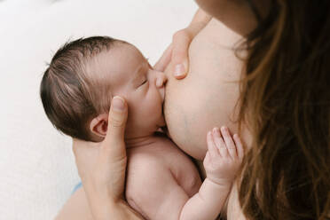 Cropped unerkennbar liebende Mutter stillt Neugeborenes beim Sitzen im Zimmer zu Hause - ADSF29447
