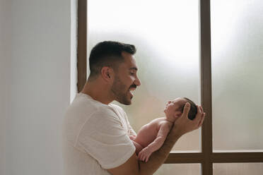 Sanftmütiger Vater mit süßem schlafenden Kleinkind in der Nähe der Wand im Fenster zu Hause - ADSF29449